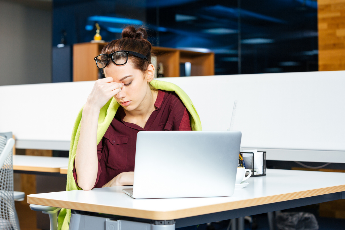 Tired beautiful young business woman in glasses working with laptop on workplace